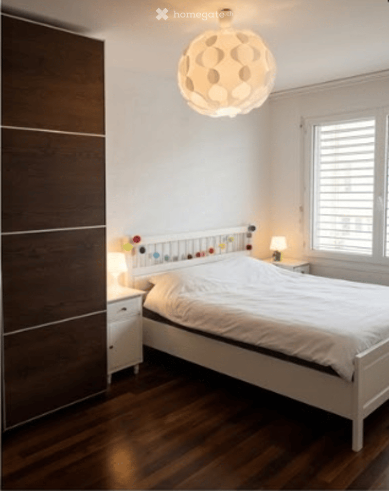 Bedroom with white bed, white nightstands, wooden floor, white walls, wooden wardrobe, lamp