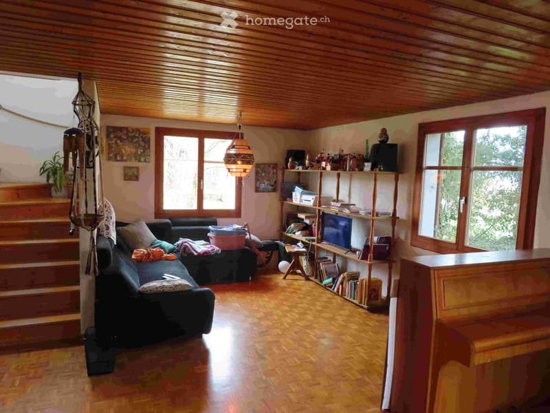 Living room with wooden floor, wooden ceiling, two couches, wooden bookshelf, TV, piano, staircase, windows