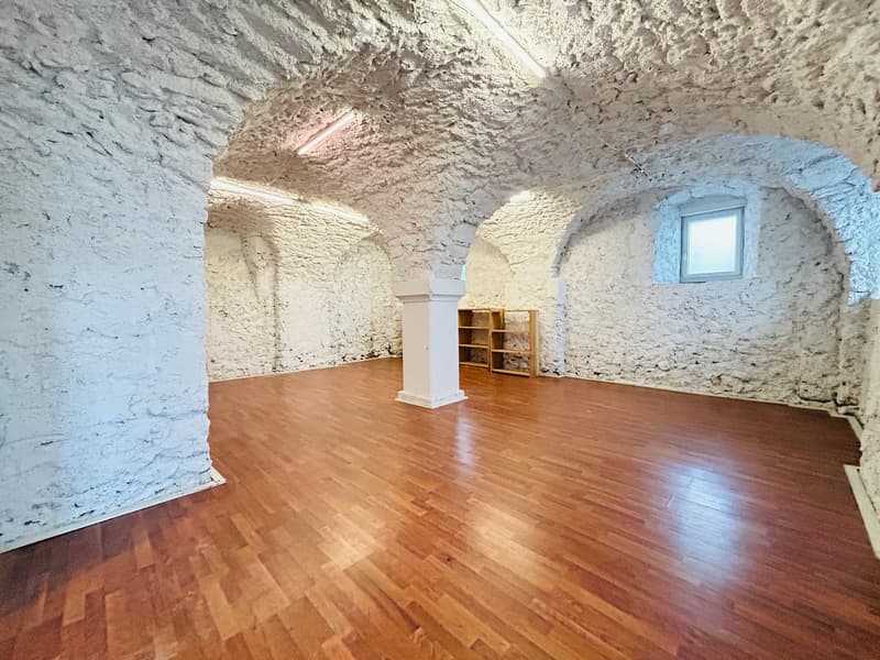 An empty room with wooden floors, arched ceiling, and white walls, there is a wooden column and a small shelf.