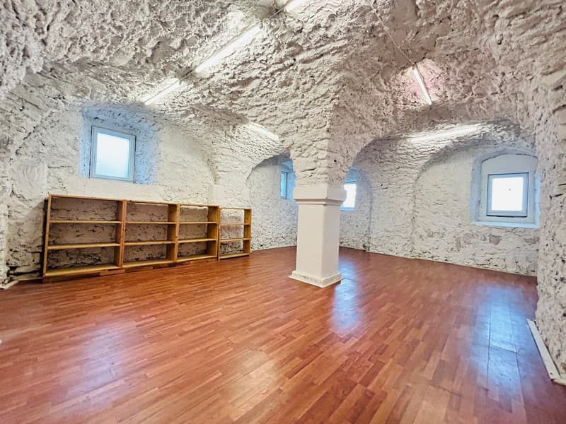 Empty room with white walls, wooden floor, three wooden shelves, three small windows, a pillar.