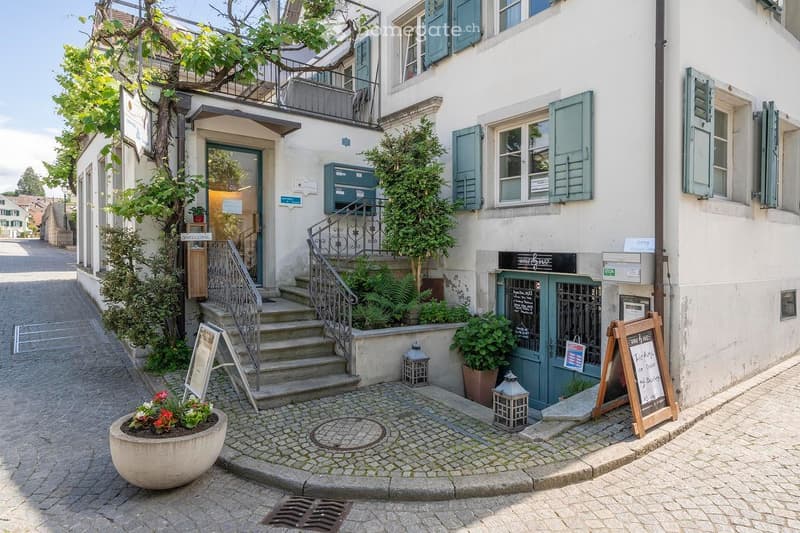 white building, green shutters, stairs, balcony, potted plants, sign