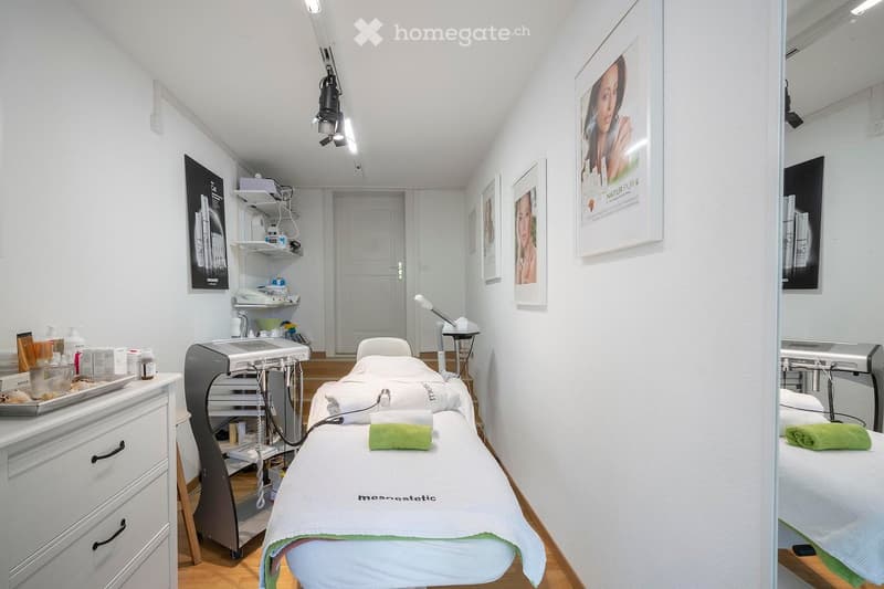 A room with a white bed, a white cabinet, a white wall, a white shelf, a white door, a white picture frame, a white towel, a green towel, a white tray, a white lamp, a white machine, and a white cabinet.
