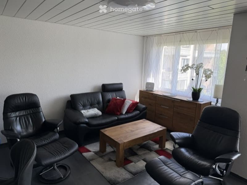 Living Room. Modern living room with black leather sofa, wooden coffee table, two black leather chairs, sideboard with a lamp and plant, and large windows with white curtains.