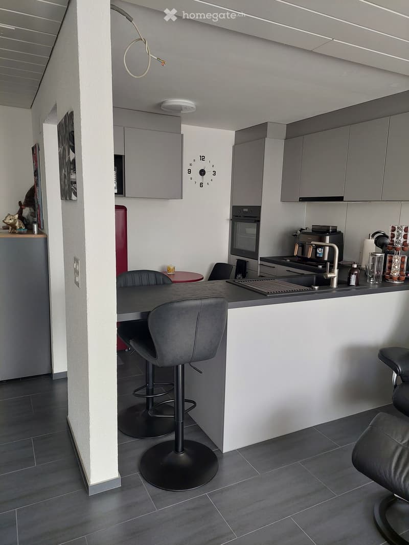 modern kitchen with island, gray cabinets, white countertops, black stools, gray tile flooring, wall clock, power outlet, small table, microwave, coffee machine, sink, faucet, oven