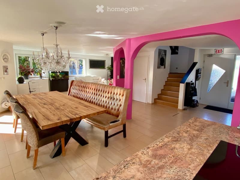 Dining area with wooden table, bench, and chairs, chandelier, pink walls, staircase, and exit sign