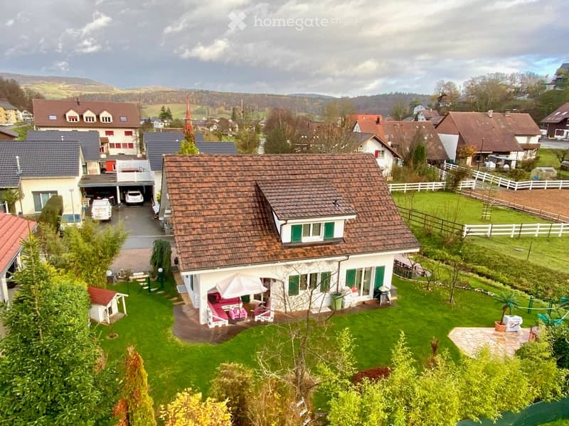 Detached house, brown roof, white walls, green shutters, driveway, garden, patio with furniture, car parked in garage