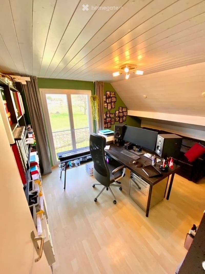 Home office with desk, computer, chair, bookshelf, couch, and window