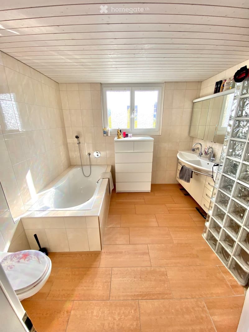 Bathroom with bathtub, sink, toilet, wooden floor, white tiles, window, mirror, cabinet, and glass wall.