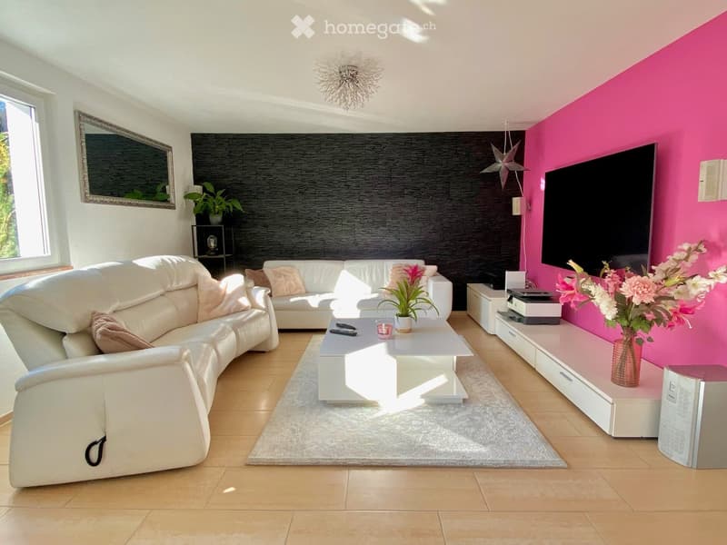 Living room with white leather couches, white coffee table, pink flowers, black wall, pink wall, TV, mirror, potted plants, wooden floor