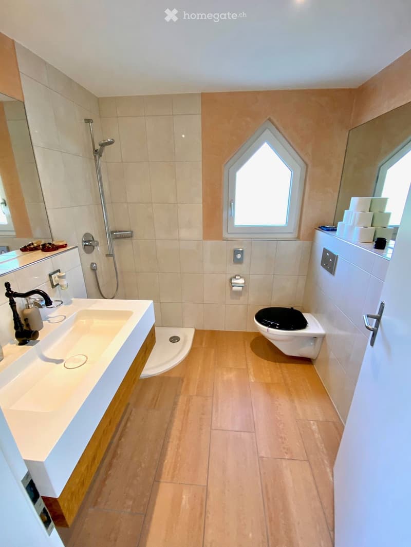 Bathroom with wooden floor, white tiles, white sink, shower, toilet, mirror, and window