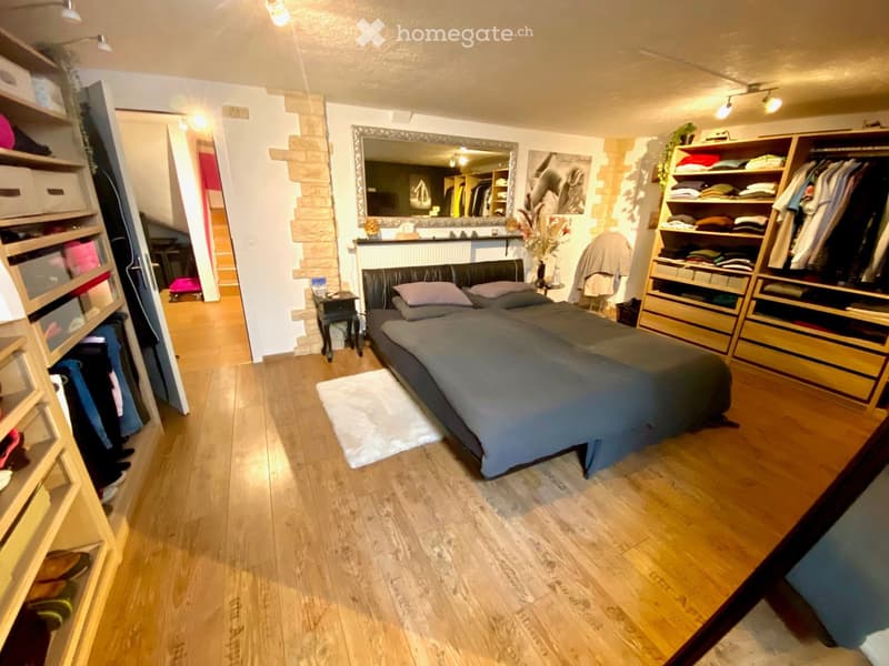 Bedroom with wooden floor, bed, mirror, wardrobe, and shelves with clothes