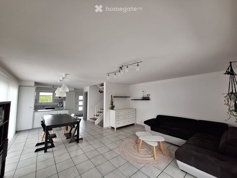 modern living room with white walls, white tiled floor, black sofa, white coffee table, white rug, white kitchen with black table and chairs, white cabinets, white staircase
