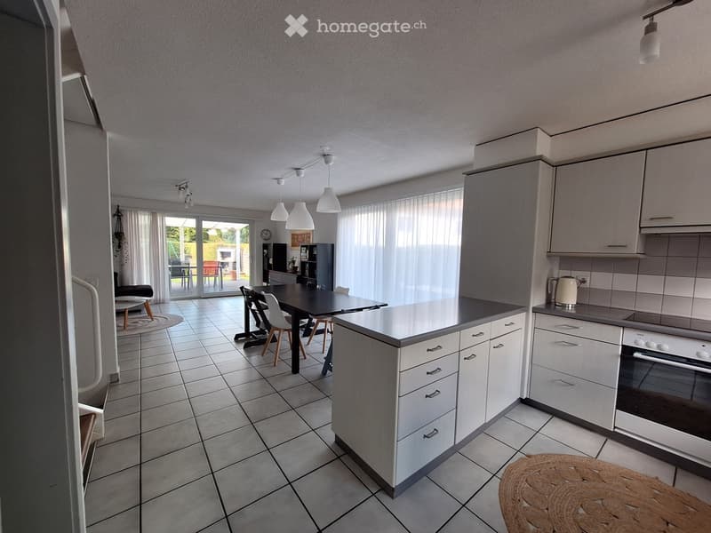 Open kitchen with dining area, white cabinets, tiled floor, modern appliances, dining table, chairs, white curtains, ceiling lights, rug, shelves, clock, picture frame, black sofa, outdoor patio with chairs and table