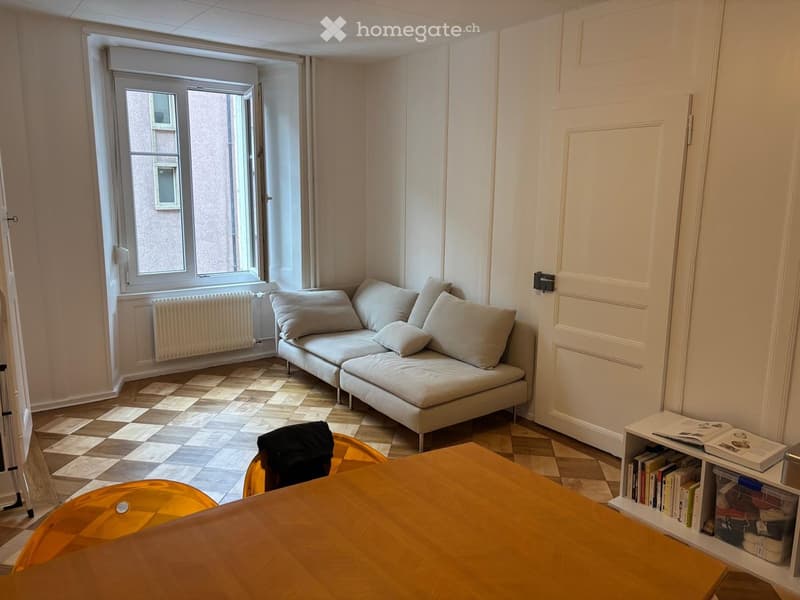 A living room with a couch, a wooden table, a radiator, and a window.