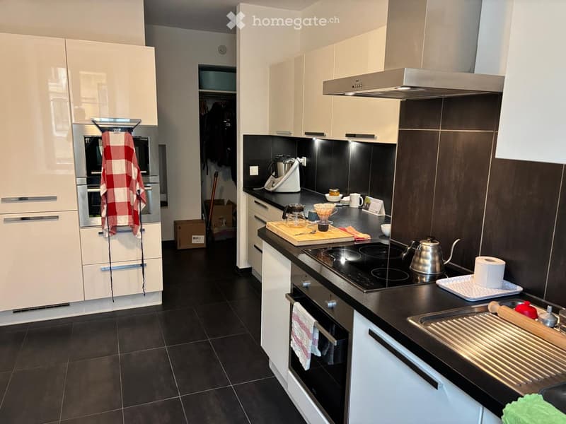 modern kitchen with black tiled floor, white cabinets, black countertops, built-in oven, dishwasher, and washing machine