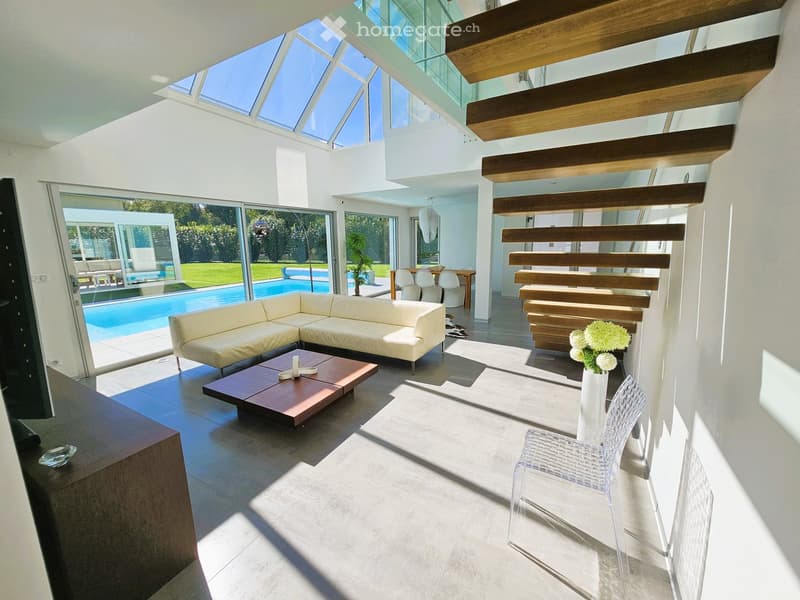 modern living room, white couch, wooden coffee table, white chair, white vase with flowers, large windows, glass door, wooden staircase, glass roof, pool view