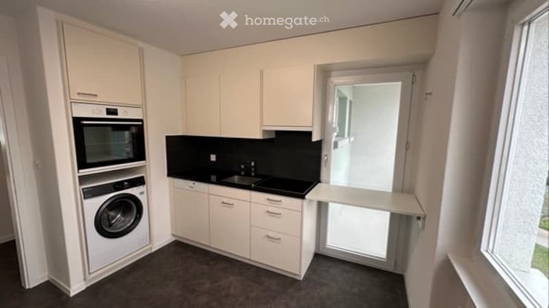 modern kitchen with white cabinets, black countertops, white appliances, window