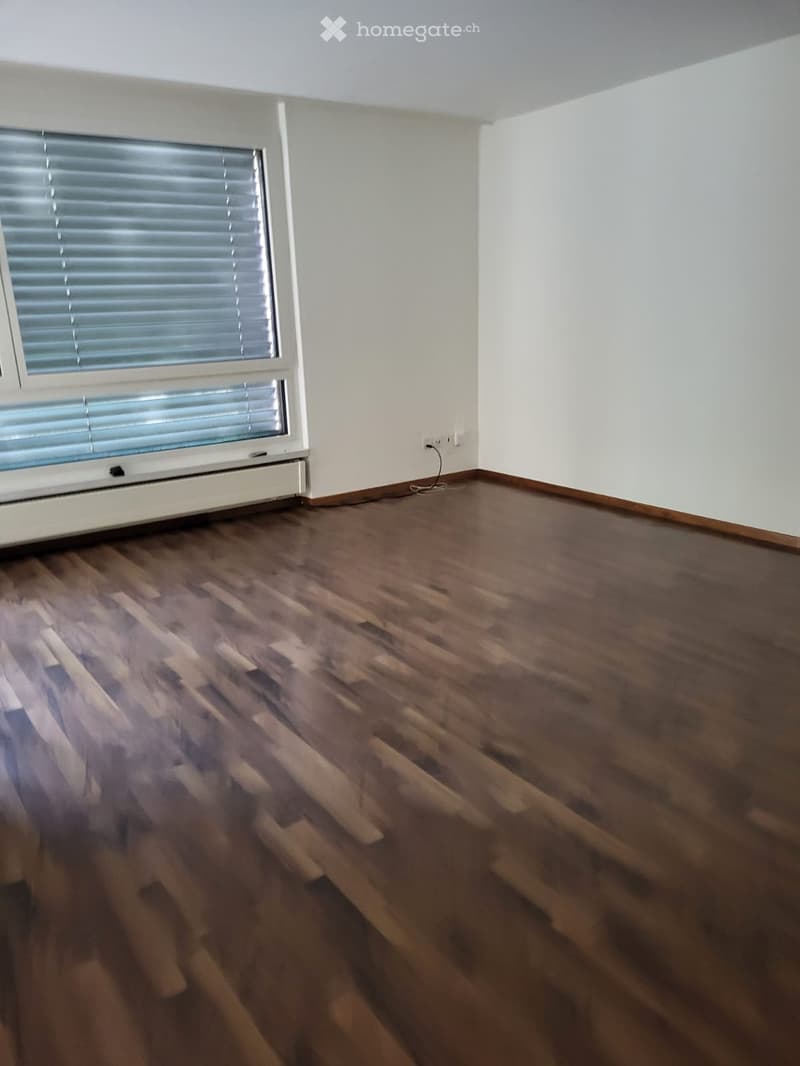 Empty room with wooden flooring, white walls, and a window with blinds.