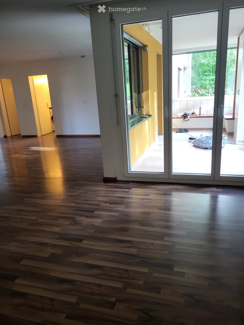 Empty room with wooden flooring, large sliding glass doors leading to a balcony, and a view of greenery outside.