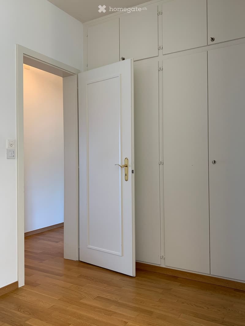 empty room with wooden floor and white walls, white door and white cabinets
