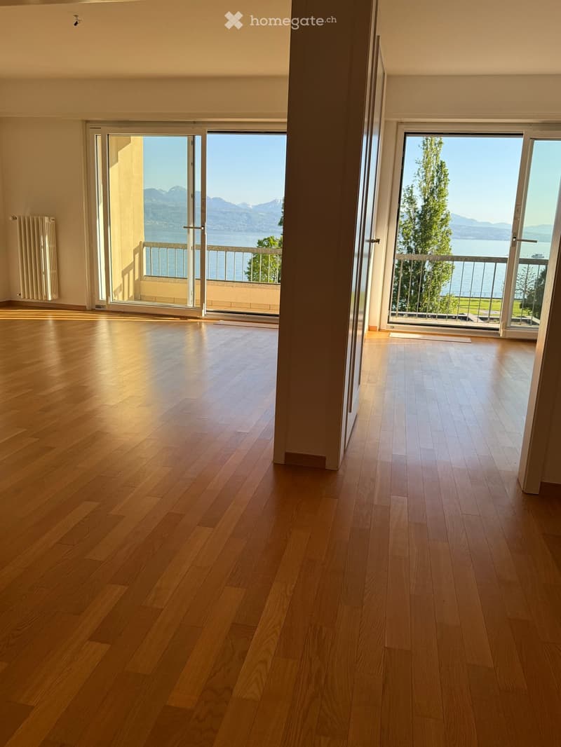 Empty room with hardwood floors, sliding glass doors leading to a balcony with a view of the lake and mountains.