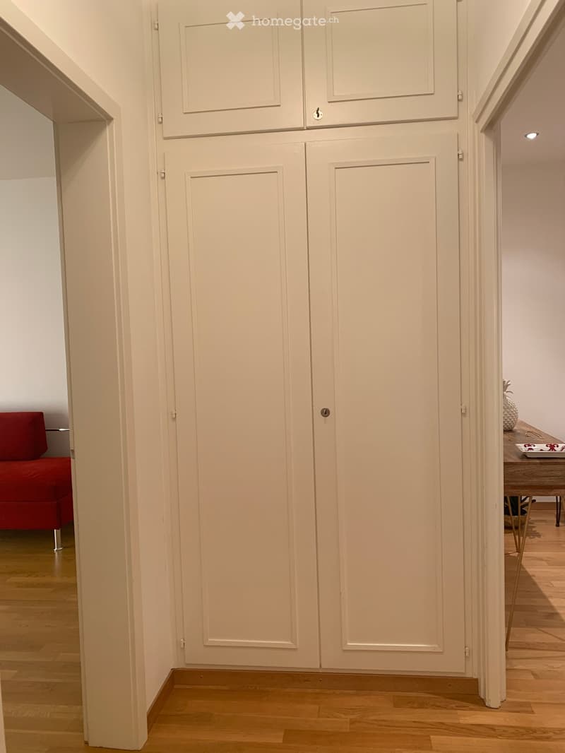 white wall, white wooden closet, wooden floor, red couch, white table with plate