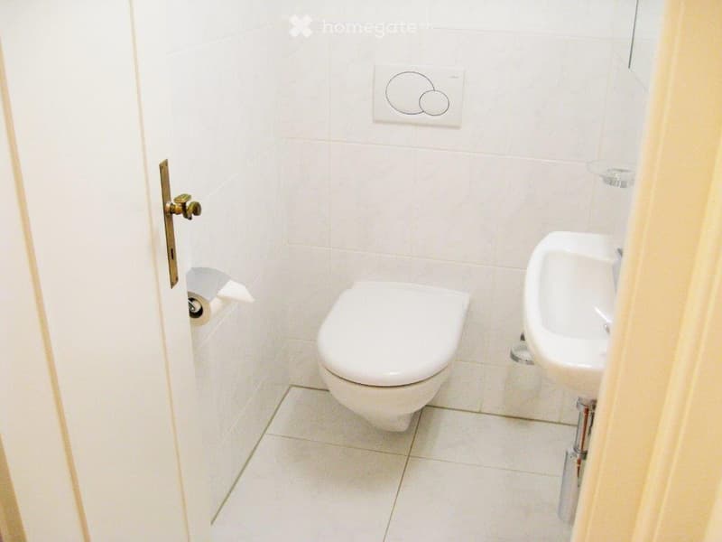 compact bathroom with white tiles, white toilet, white sink, toilet paper holder, wall mounted toilet flusher