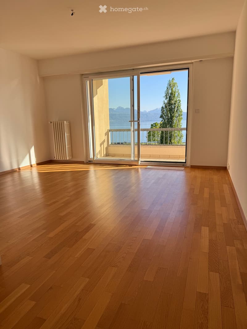 Empty room with hardwood floors, large sliding glass doors leading to a balcony with a view of the lake and mountains.