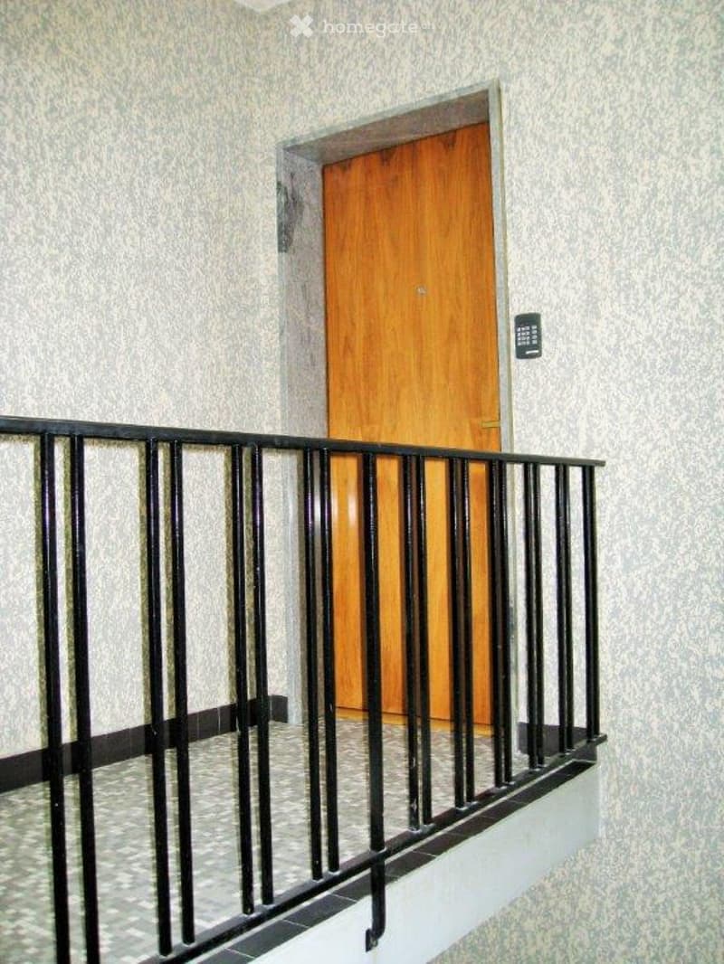 small balcony with black railings, tiled floor, wooden door