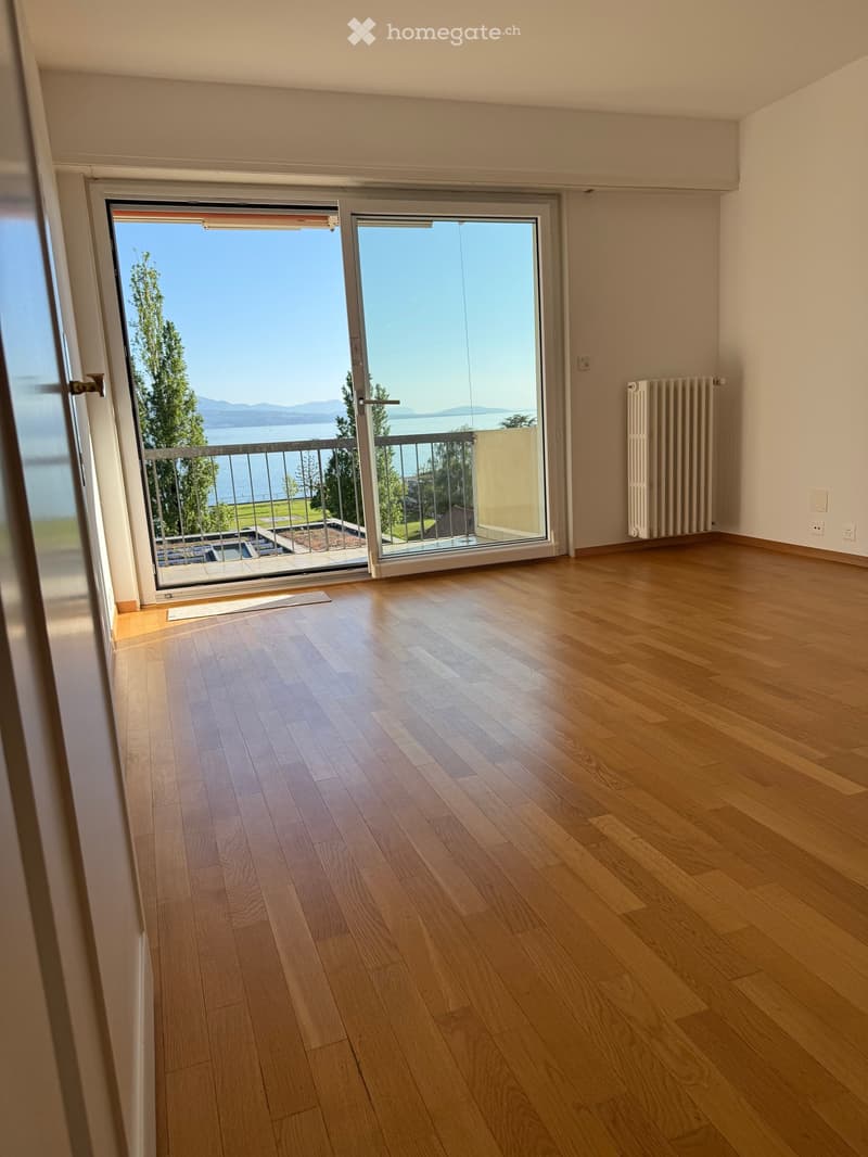 Empty room with hardwood floors, sliding glass doors leading to a balcony with a view of the sea and mountains.