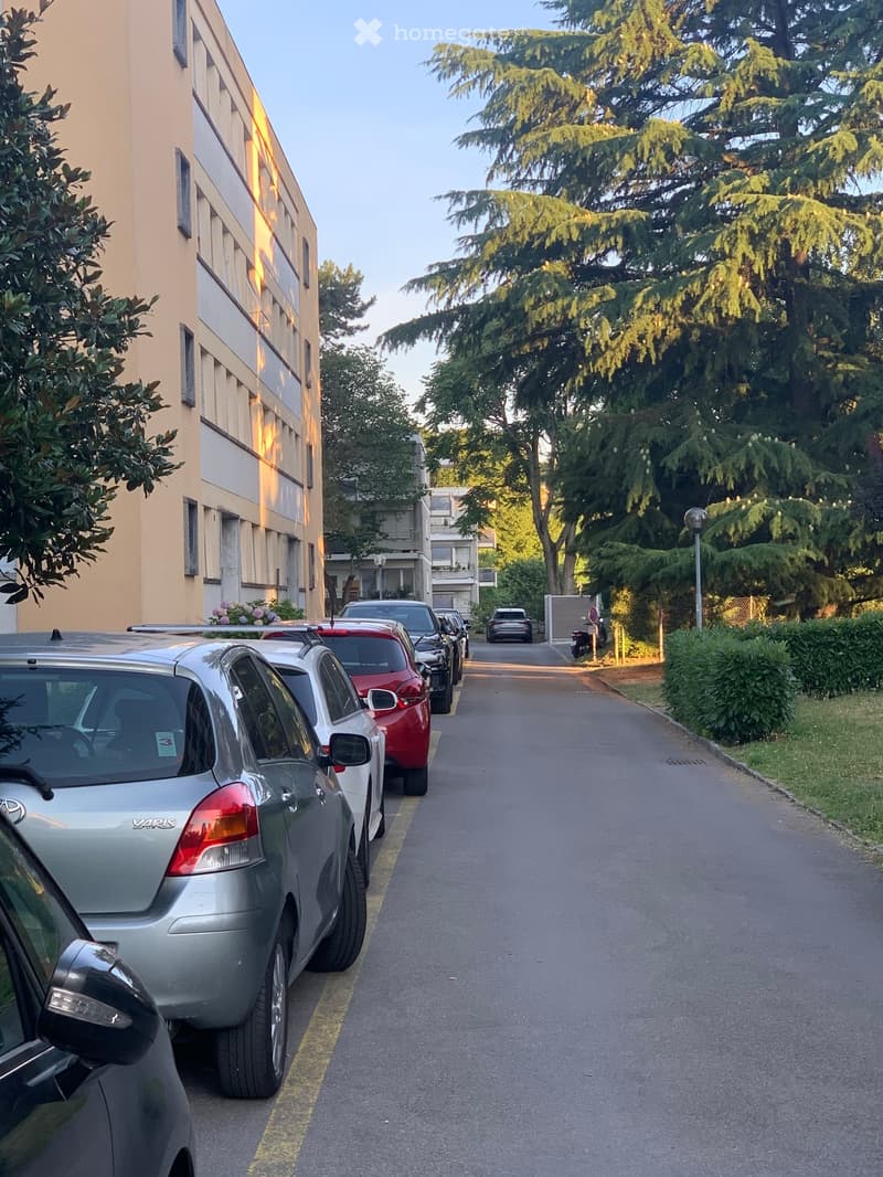A line of cars parked along a street beside a beige building.