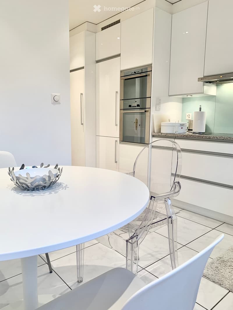white kitchen with white tile floor, white marble counter, stainless steel oven, round dining table, clear plastic chair, white dining chair
