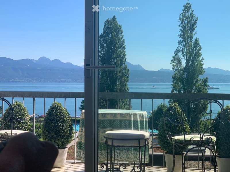 chairs and tables on balcony, green tablecloth, metal railing, view of mountains and lake