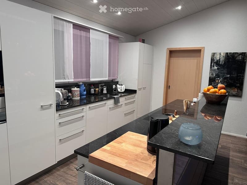 modern kitchen with white cabinets, black countertops, wooden floor, kitchen island with cutting board, coffee maker, and bowl of fruit