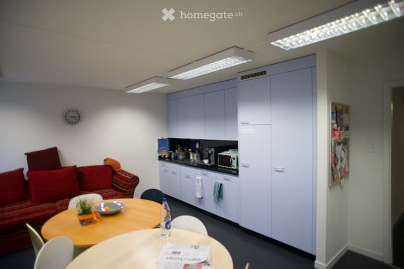 modern kitchen with white cabinets, black countertop, microwave, coffee machine, dining table, couch, clock, plants