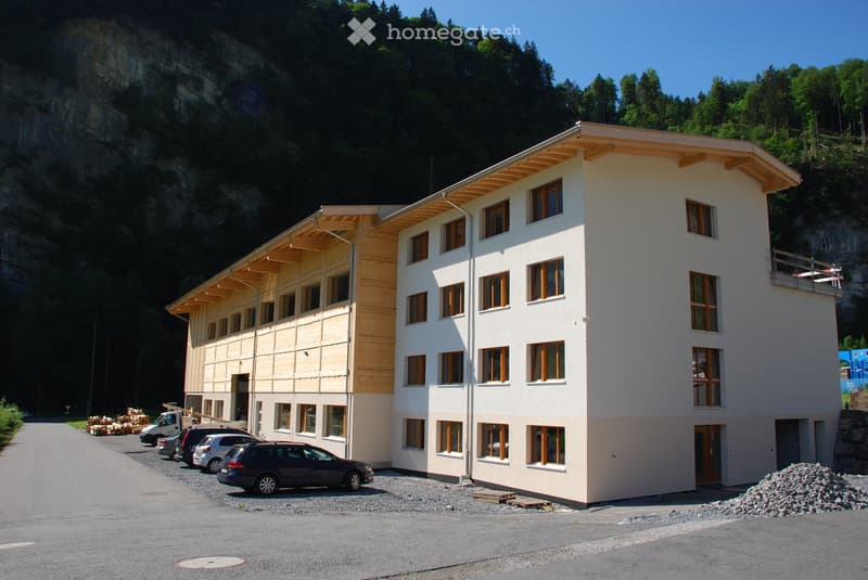 multi-story residential building, wood trim on first floor, multiple cars parked in front