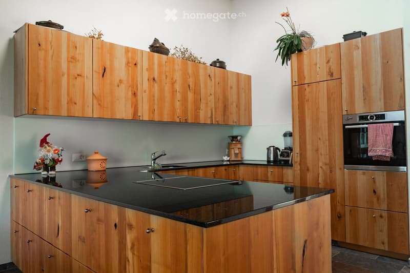 Wooden kitchen with granite countertop, stainless steel sink, wooden cabinets, stove, microwave, kettle, coffee grinder