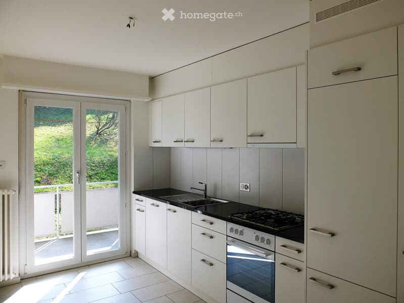 modern kitchen with white cabinets, black countertops, stainless steel appliances, sliding glass doors to balcony