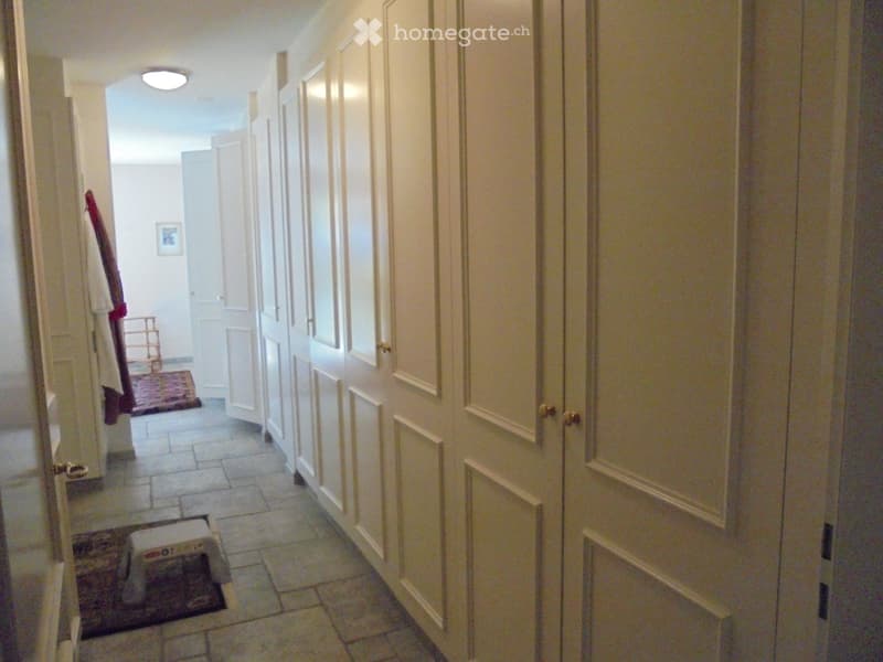 A hallway with white doors, tiled floor, and a row of white cabinets with gold knobs.