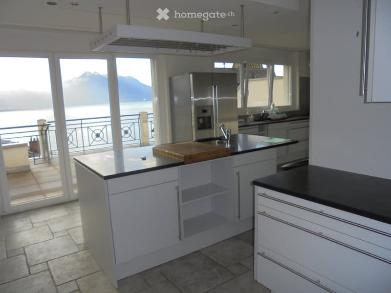 modern kitchen, white cabinets, black countertops, stainless steel refrigerator, large windows, balcony with railings, tiled floor