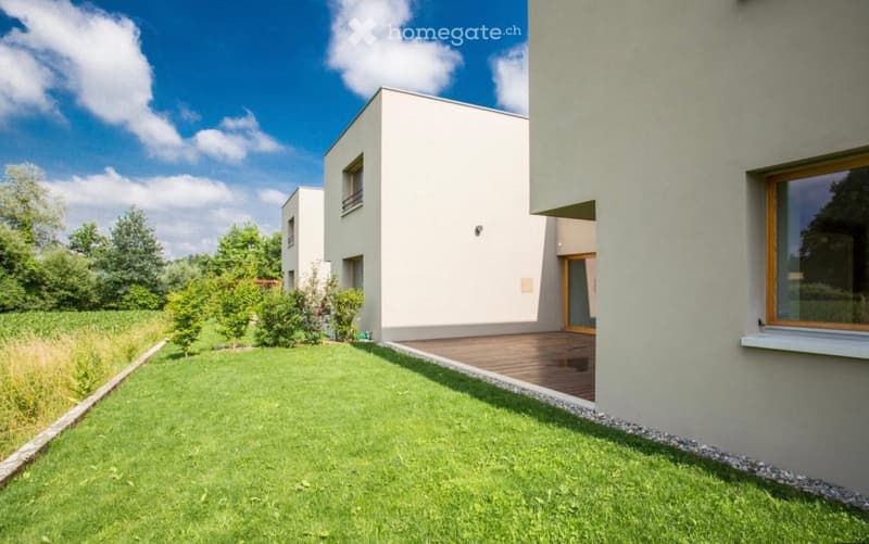 Modern house, white exterior, wooden deck, large windows, well-manicured lawn, surrounding greenery