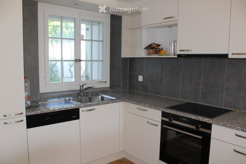 modern kitchen with white cabinets, granite countertops, stainless steel sink, dishwasher, oven, and a window with a view of the outside