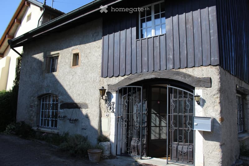 Stone house, black wooden shutters, black metal gate, lamp on both sides of the gate, mailbox on the right side of the gate