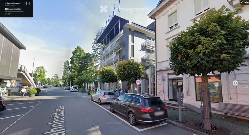 Street with parked cars, trees, and buildings on both sides.