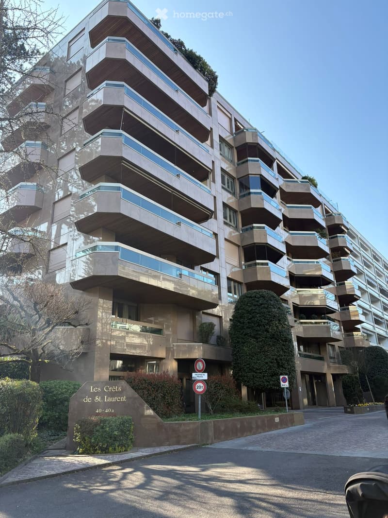 Modern apartment building with multiple floors, glass balconies, and a landscaped entrance.