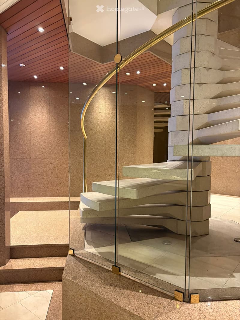 Modern staircase with glass railing and gold handrail, concrete steps, glass walls