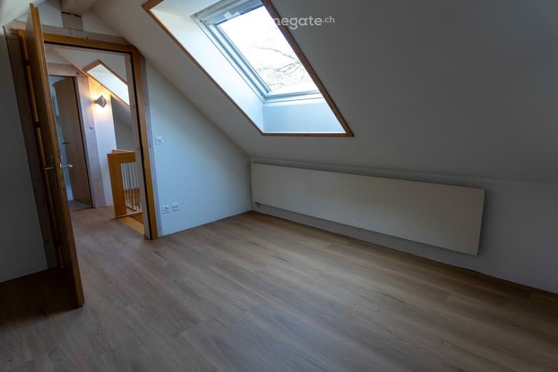 Wooden floor, two windows, a radiator and a door leading to another room