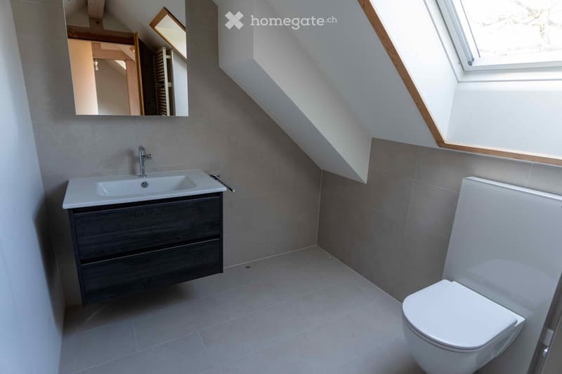 Attic bathroom, under sloped ceiling, mirror, toilet, sink, tiled walls, natural light from window