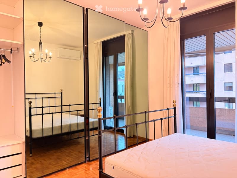 Bedroom with two beds, large mirror, chandelier, wooden floor, balcony with view