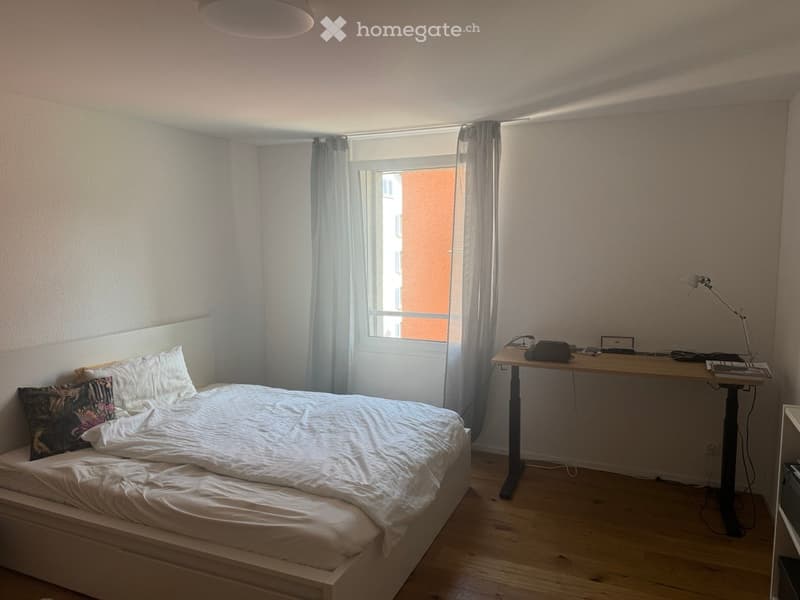 A bedroom with a bed, desk, lamp, and window with curtains.